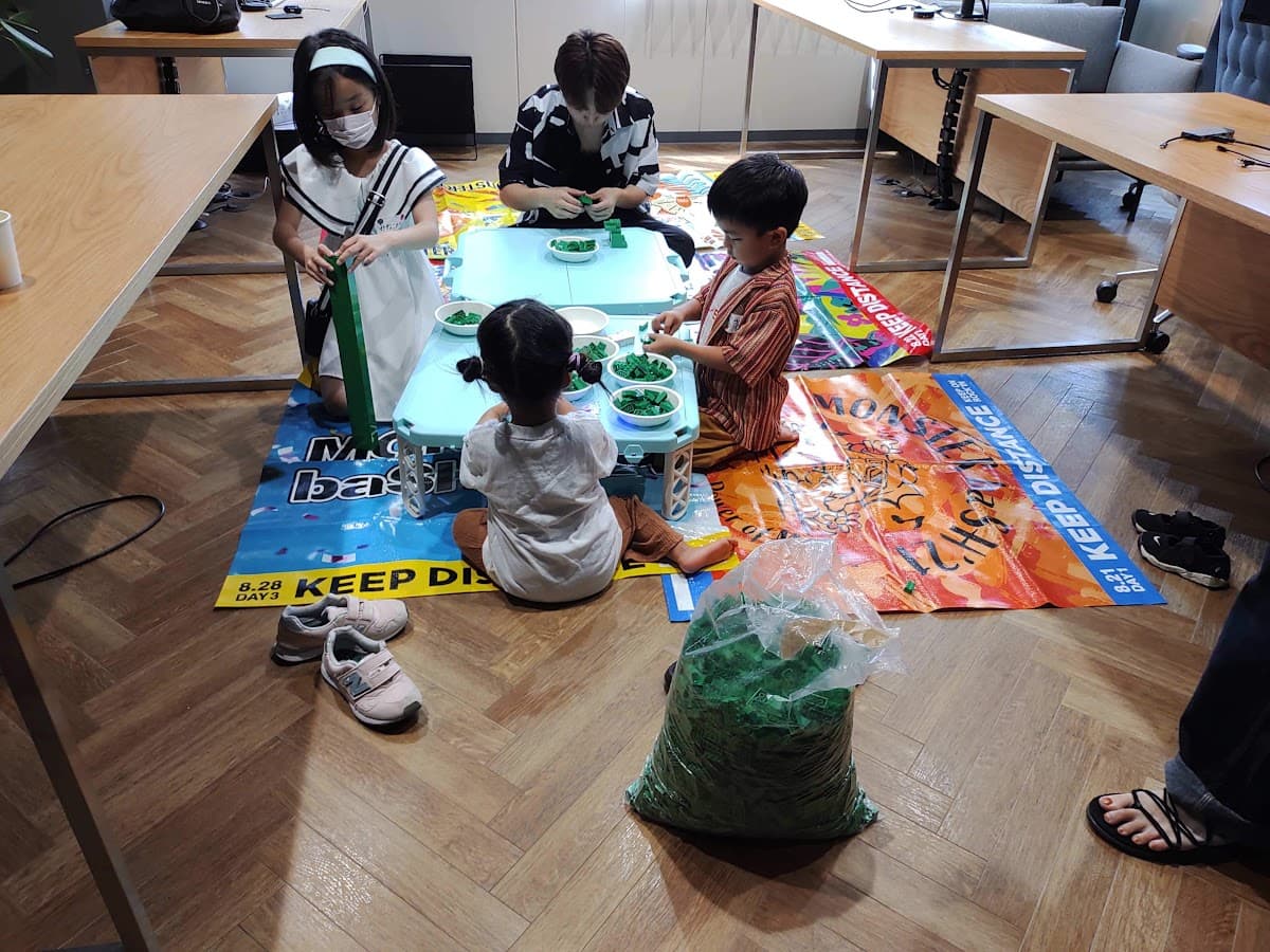 青いテーブルを囲んで、大人と子どもがブロックを組み立てる様子